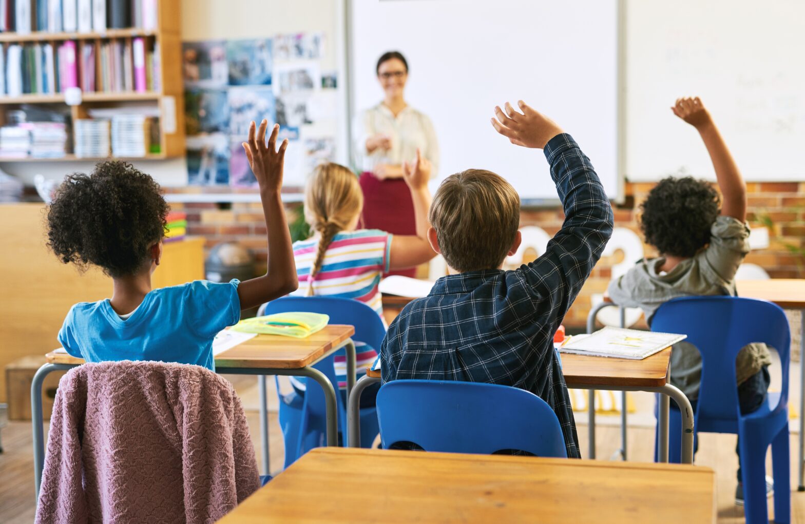 Imagen de una clase con niños levantando la mano.