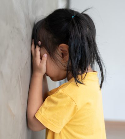 Niña tapándose la cara frente a la pared mostrando frustración o bloqueo emocional en el aula.