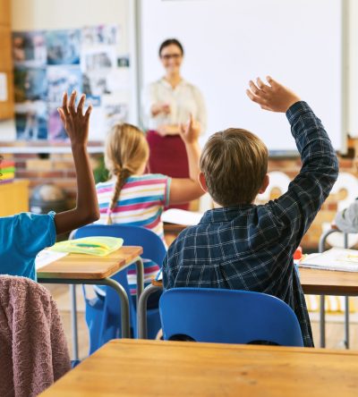 Imagen de una clase con niños levantando la mano.