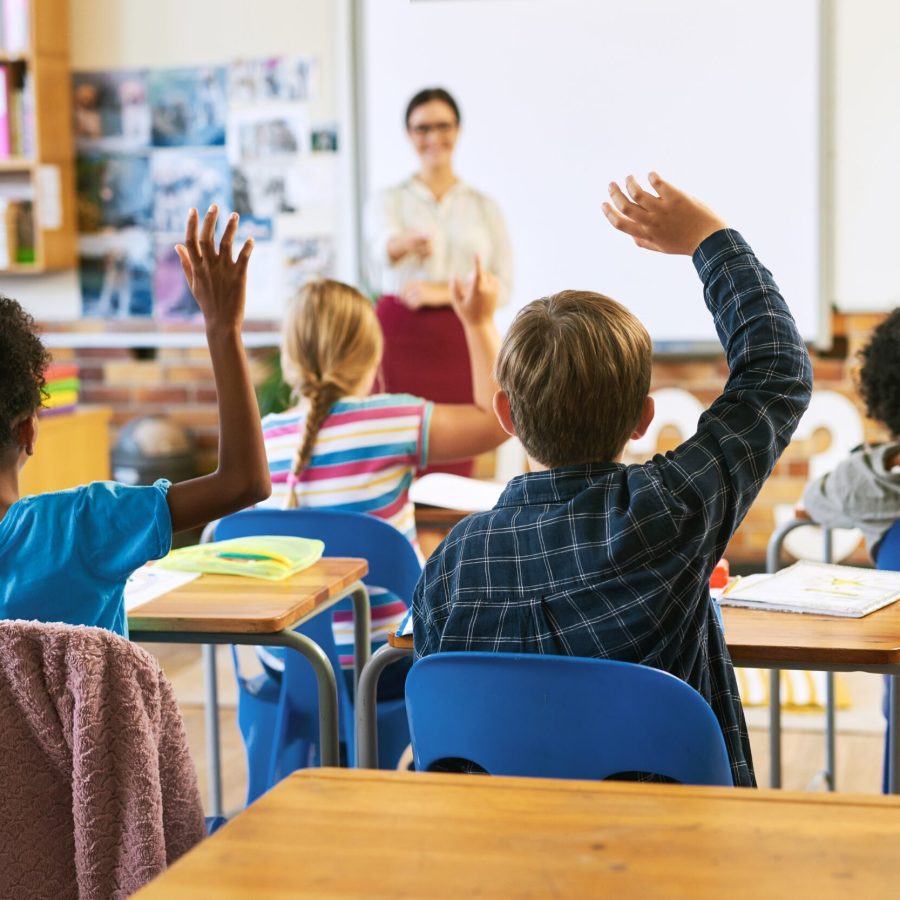 Imagen de una clase con niños levantando la mano.